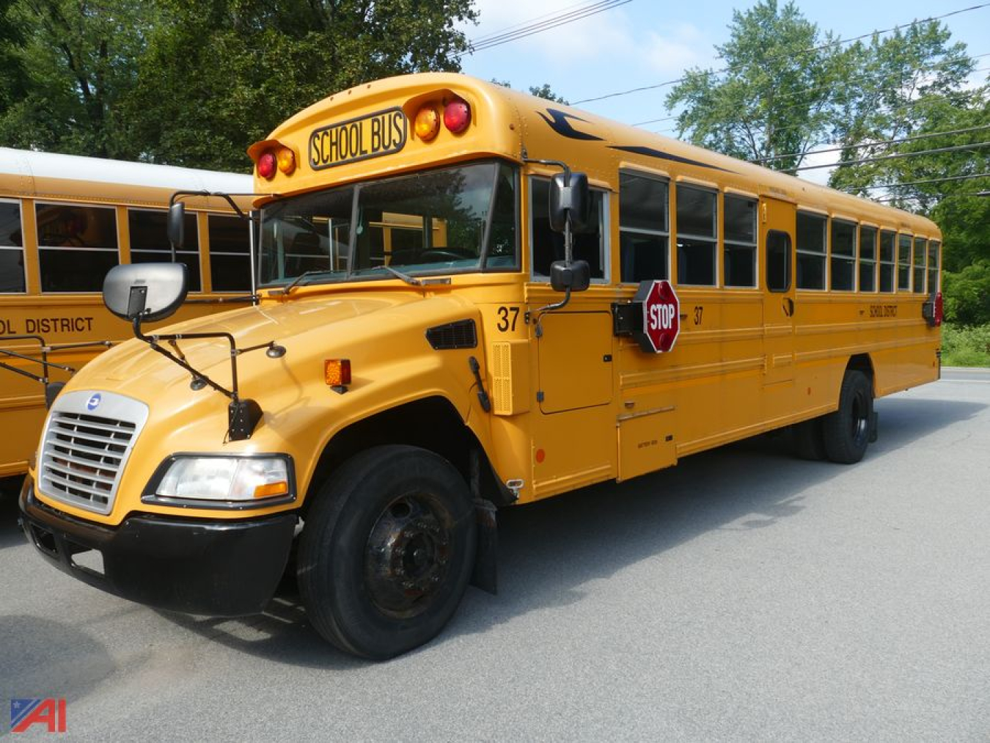 Yellow 2014 Blue Bird Vision school bus in service with stop sign extended, 'SCHOOL BUS' sign on front, black bumper, black wheels, side doors and windows along the bus.