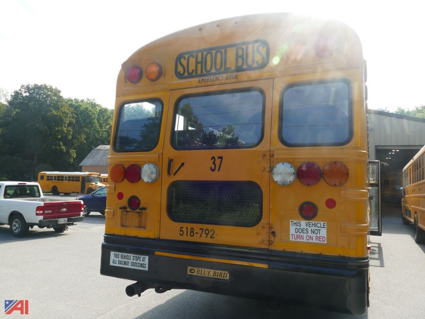Rear view of a yellow 2014 Blue Bird Vision school bus with number 37, rear lights, access panel, and Blue Bird badge; signs indicate turn on red and school bus markings.