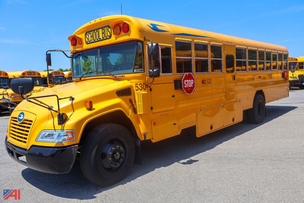Yellow 2018 Blue Bird Vision school bus side/front view showing STOP sign, warning lights, and Windows