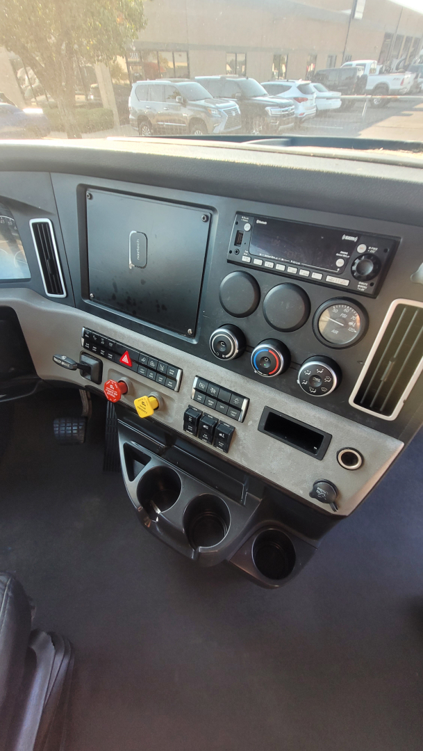 Truck cockpit dashboard with multiple gauges and controls; central display with radio, climate controls, hazard switch, and cup holders visible.