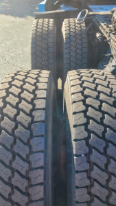 Dual rear axles of a Freightliner Cascadia 126 tractor showing aggressive tread on dual tires and the frame between wheels.