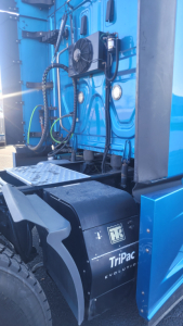 Truck side view showing TriPac Evolution auxiliary power unit housing and fuel lines on blue Freightliner Cascadia frame.