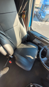 Vehicle cab interior showing driver seat and steering wheel of a Freightliner truck in a showroom lot.