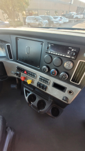 Truck cockpit dashboard with multiple gauges and controls; central display with radio, climate controls, hazard switch, and cup holders visible.