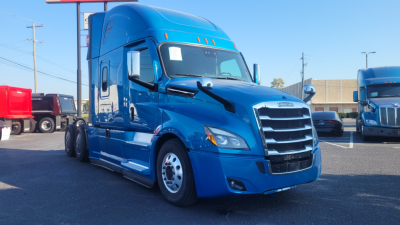 Blue Freightliner Cascadia 126 semi-truck in a dealership lot, front view with other trucks in background.