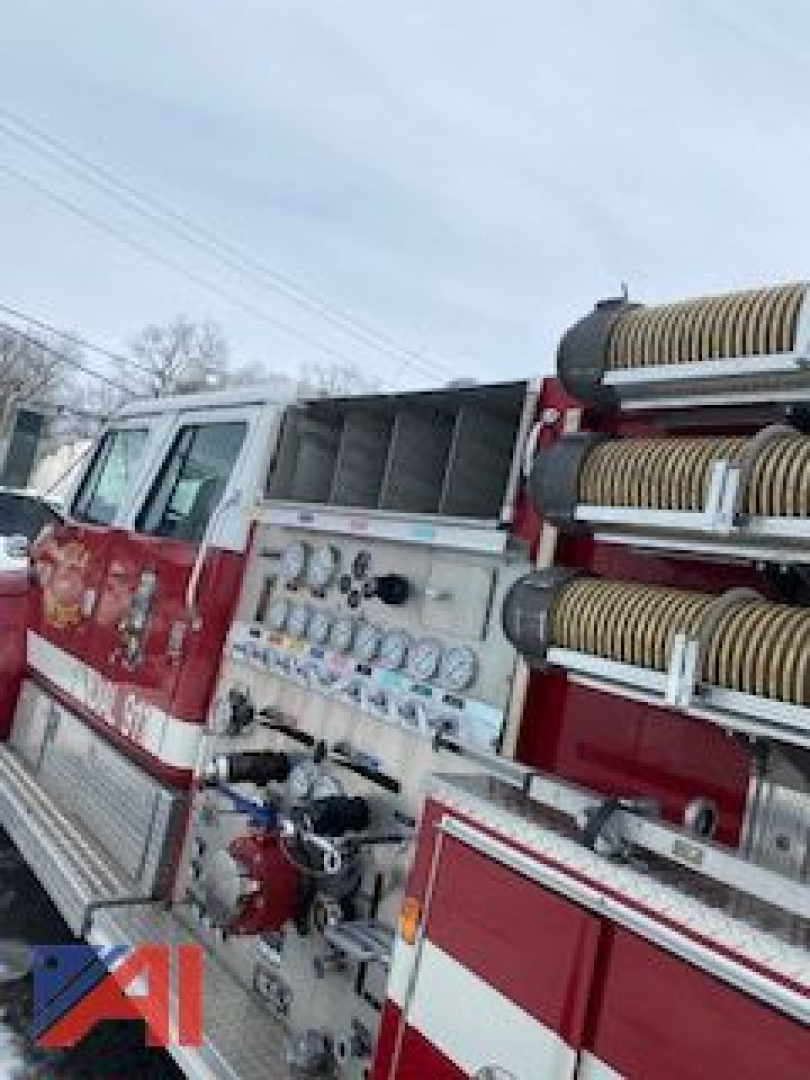 Fire engine/pumper side showing gauges, hoses, and compartments on a red and white International conventional cab fire truck.
