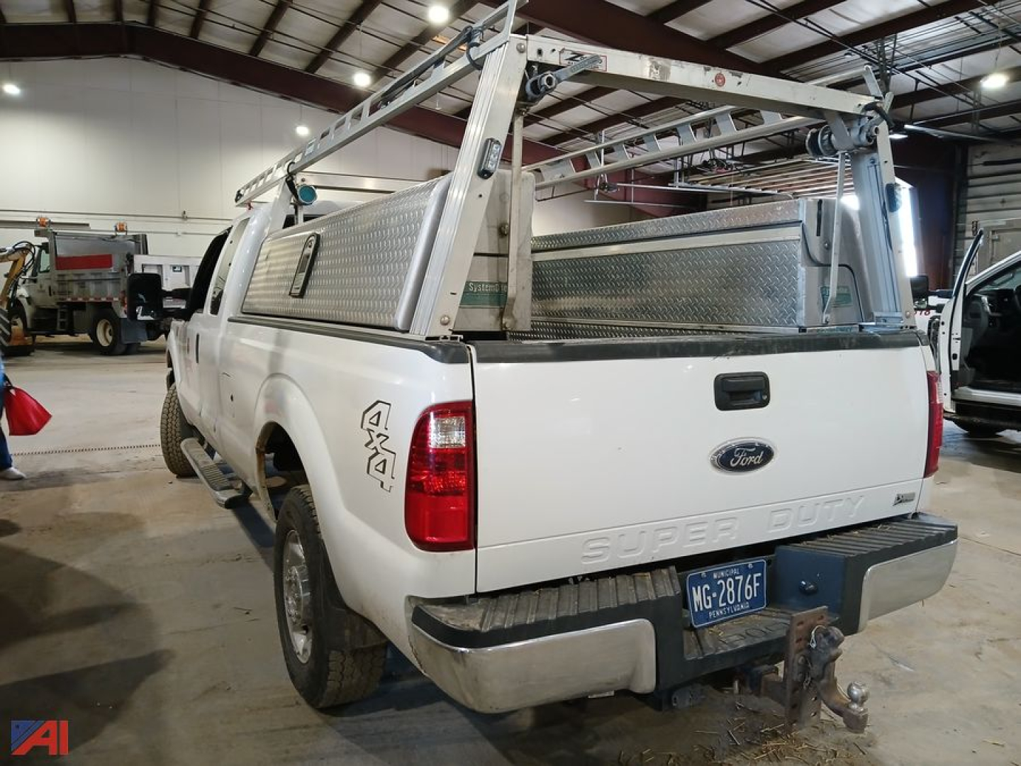 Ford F-250 Super Duty pickup tailgate view with aluminum ladder rack and toolbox, rear bumper hitch, white paint, dealership environment.