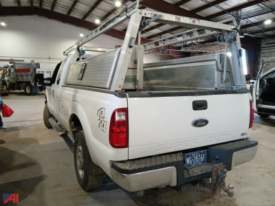 Ford F-250 Super Duty pickup tailgate view with aluminum ladder rack and toolbox, rear bumper hitch, white paint, dealership environment.