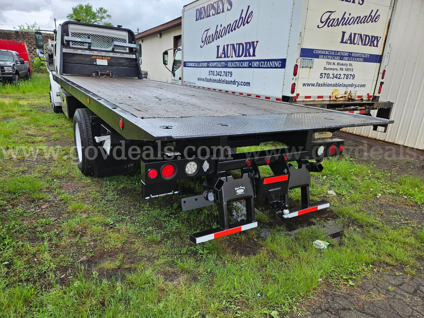 Freightliner M2 106 flatbed tow truck rear view showing hitch assembly, taillights, and mudflaps with reflective bars.
