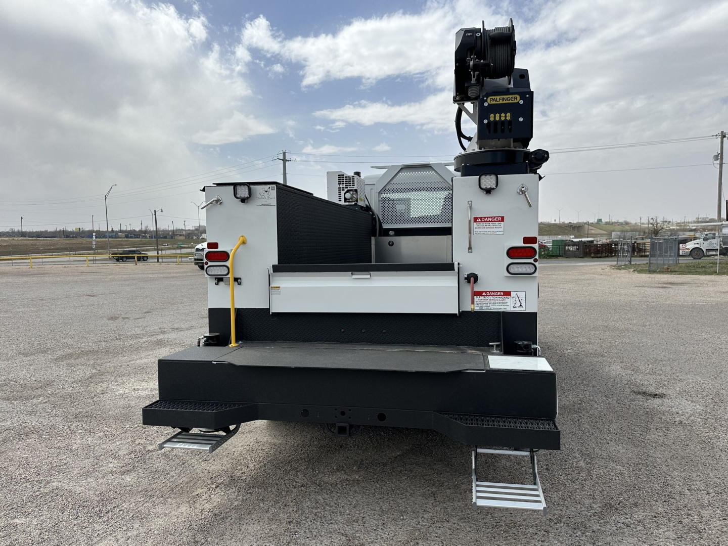 Equipment rear view of a 2025 Mack MD7 service truck showing crane, l-shape steps, and white body.