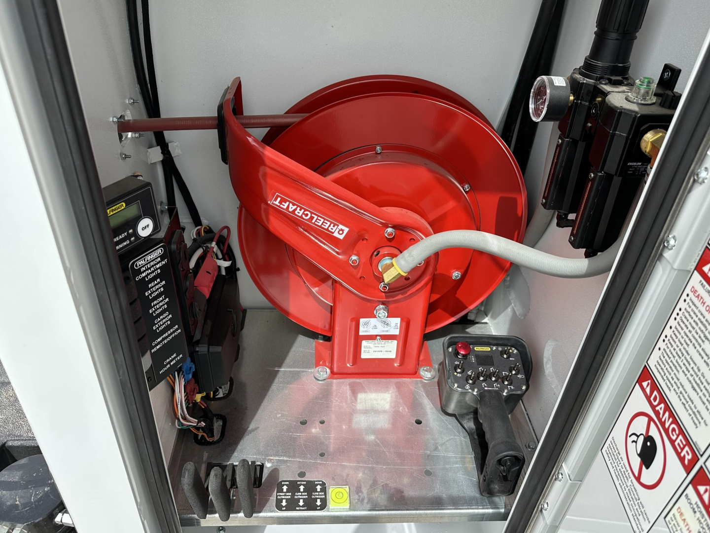 Mack MD7 service truck equipment bay showing red air reel and hydraulic control components, with black electrical box and warning labels.