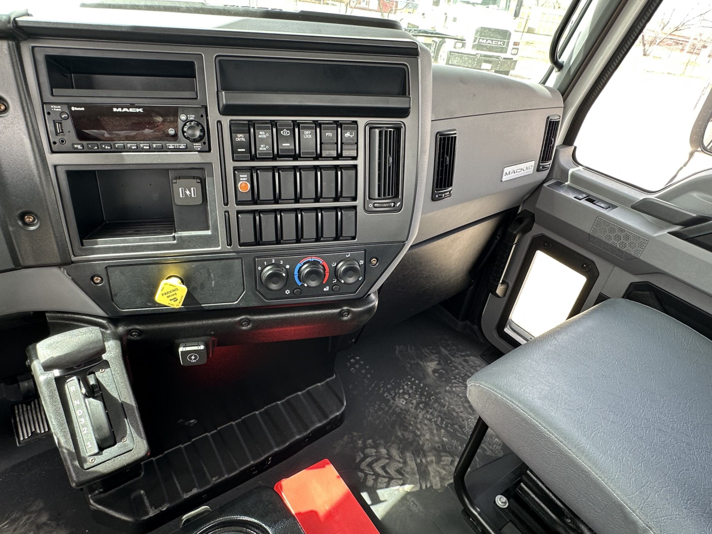 Panel of a 2025 Mack MD7 cab showing dashboard controls, radio, vents, climate controls, and passenger seat.