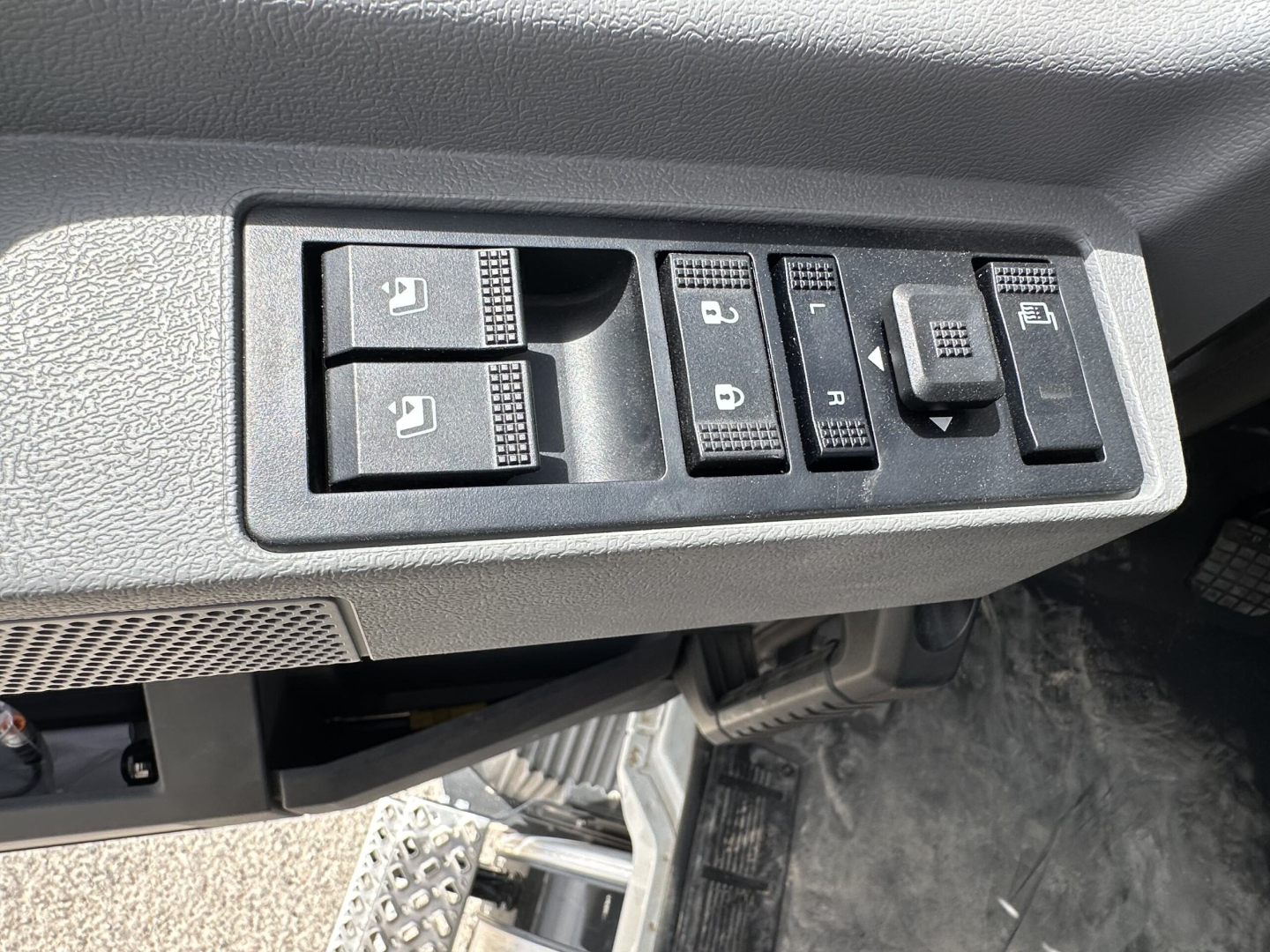 Dashboard control switches and window/mirror controls in a Mack MD7 truck cab showing multiple toggles and textured buttons.