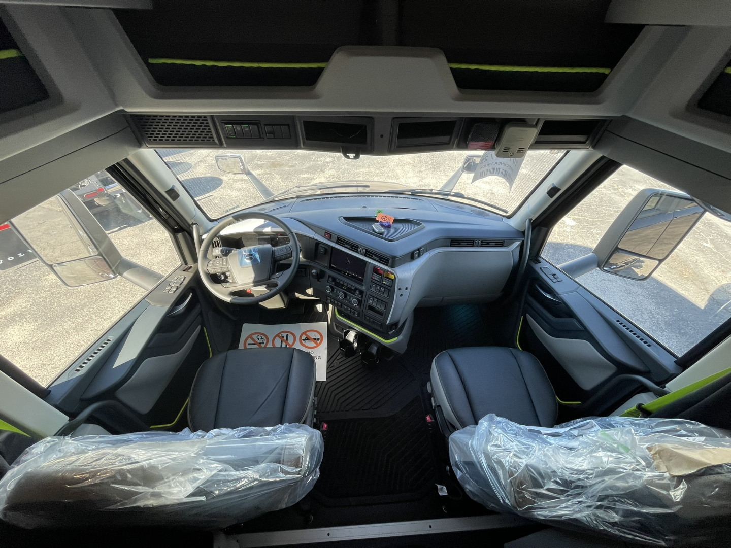 Volvo VNL64T860 cabin view showing steering wheel, dashboard, and front seats with protective plastic on seat covers.