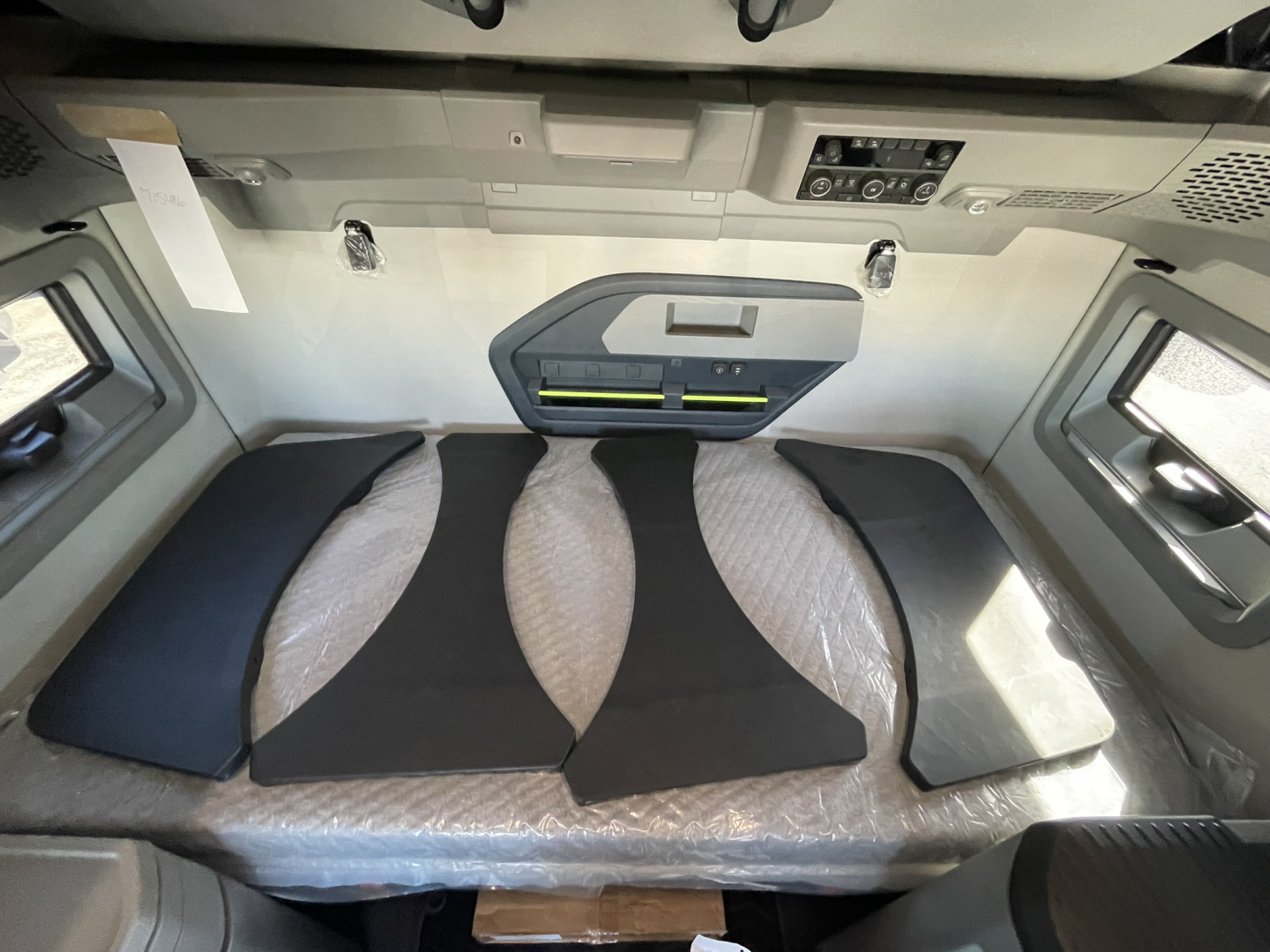 Volvo VNL64T860 sleeper cab interior showing bed platform with dark cushions and overhead dashboard panel.