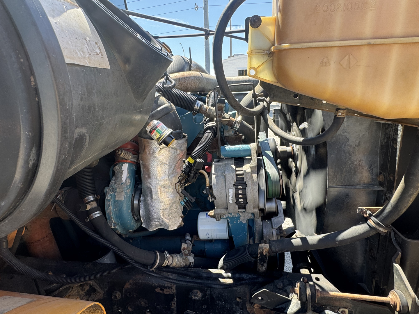 Engine bay of a 2000 International Navistar 3800 showing hoses, belts, alternator, and coolant reservoir.