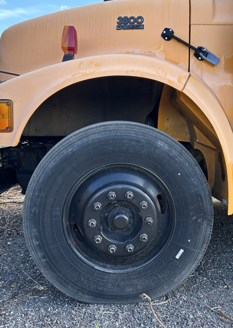 Front quarter-view of a yellow International 3800 bus showing front wheel with hub and fender, and partial body badge reading 3800 International.