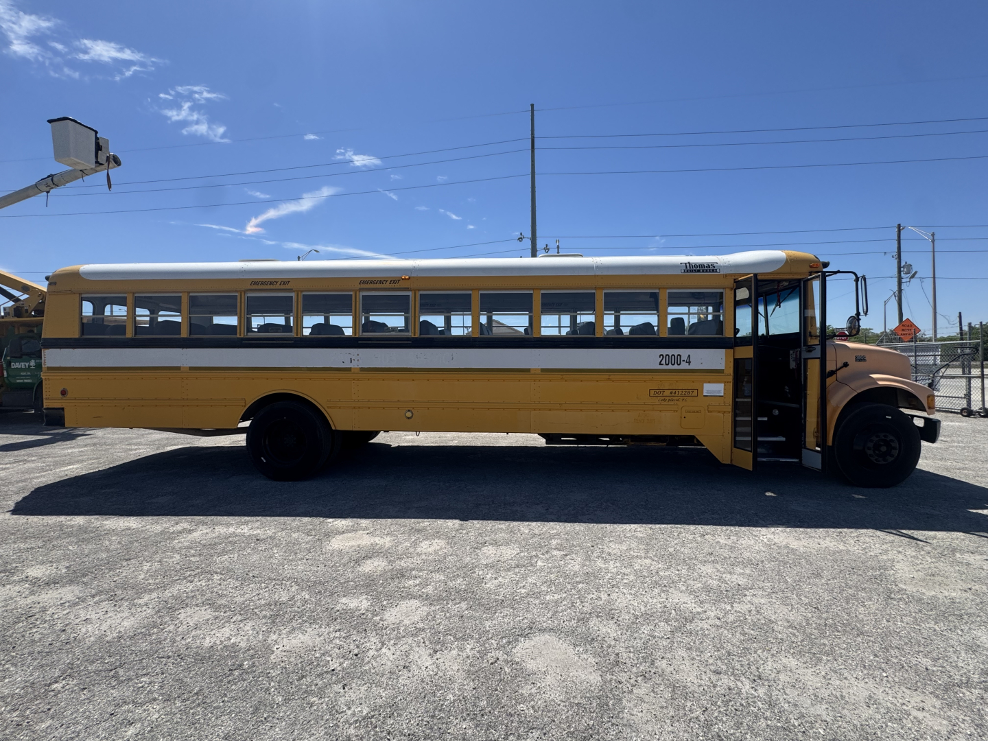 School bus side view showing a yellow and white International Navistar 3800 with black stripe, number 2003-4 near rear, open door at front, chrome hubcaps.
