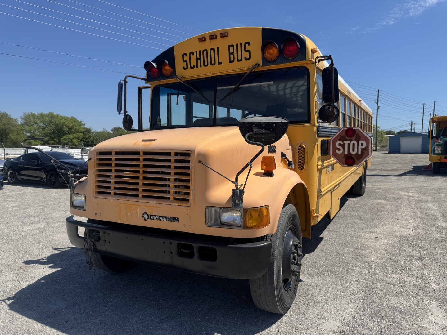 School bus front-left view showing yellow 2000 International Navistar 3800 with STOP sign, school bus lettering on hood, and utility mirrors.