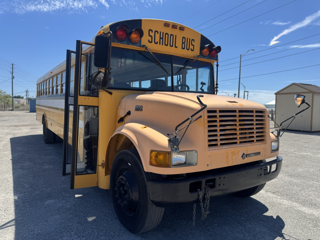 Front-left view of a yellow school bus with open door, 'SCHOOL BUS' sign, and international logo on the grille.