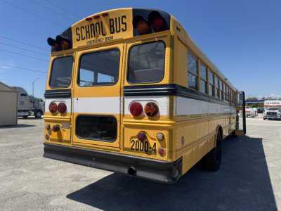 Bus rear view showing yellow International/Navistar school bus with emergency exit door, red tail lights, and '2000-4' marking.