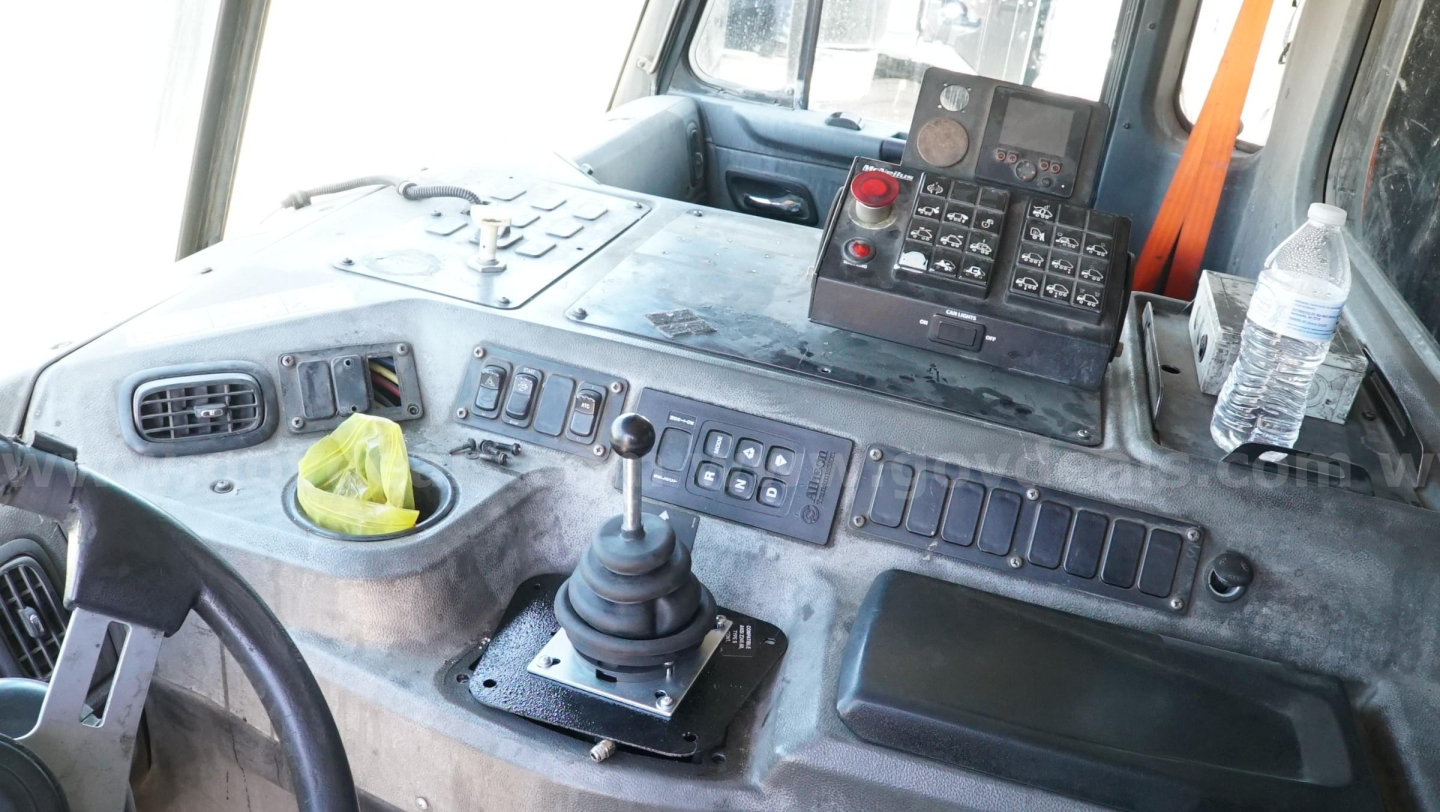 Truck cab interior showing gear shifter, control panel, and radio; various switches and a water bottle on the dash.