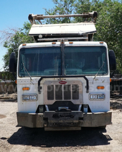 Front view of a white 2015 Peterbilt 320 garbage truck with a raised hydraulic loader, grille, and bumper, in-service condition.