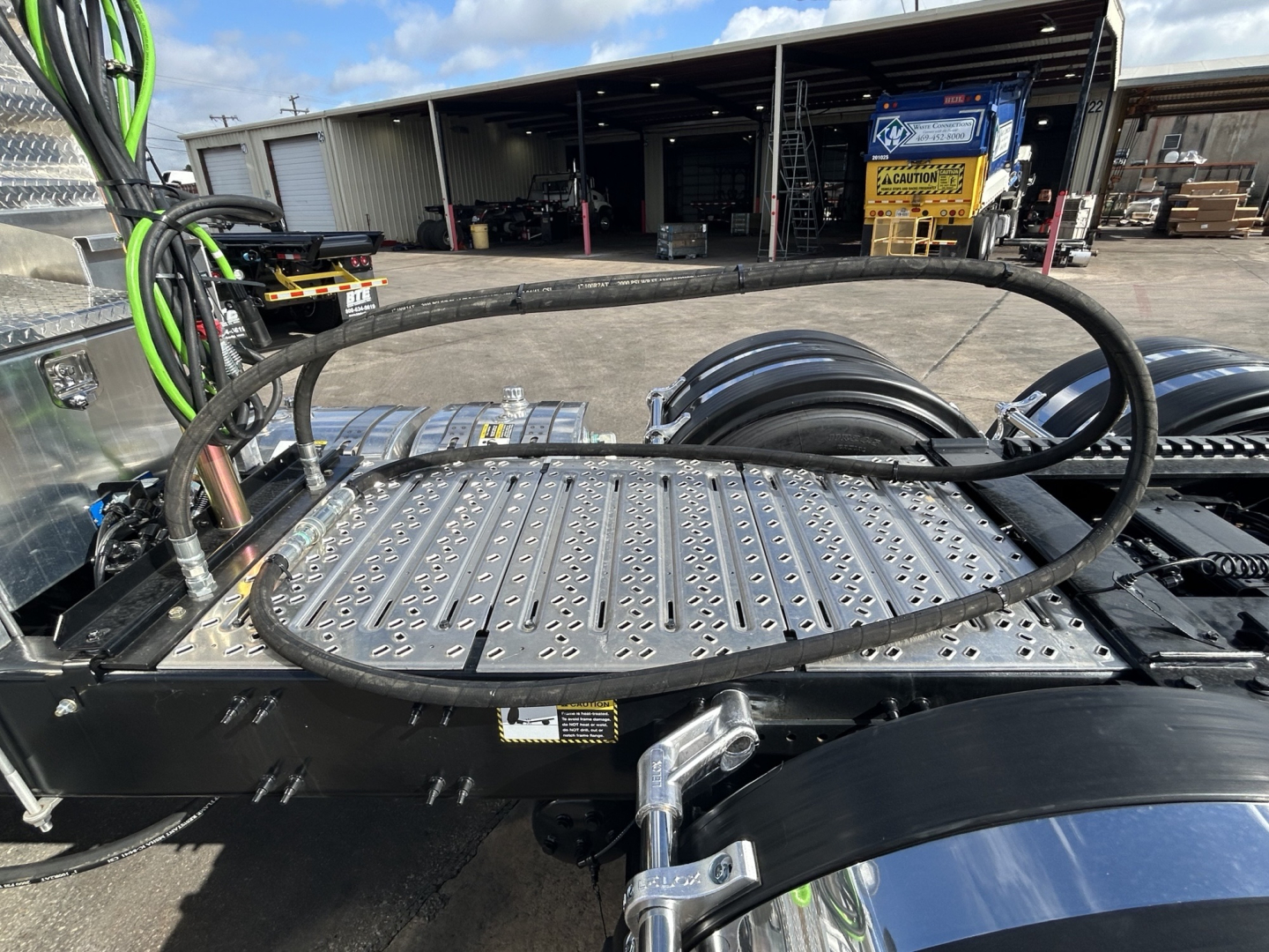 Truck cab area showing a metal deck and hoses on a Mack GR84FT chassis, with twin rear wheels and a large black coiled hose loop over the deck.