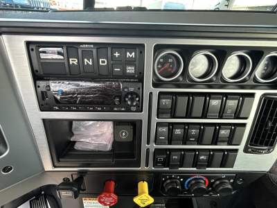 Truck dash area showing gear selector R N D + M, multiple round gauges, control panels and switches, Mack GR84FT interior details.