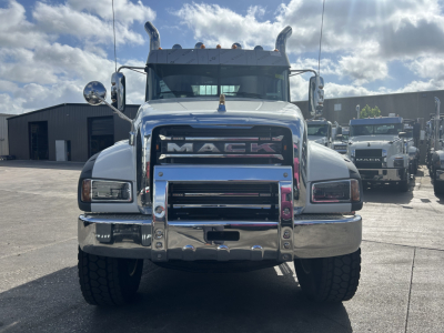 Front view of a white Mack truck with large grille and chrome bumper showing MACK emblem; daytime outdoor lot.