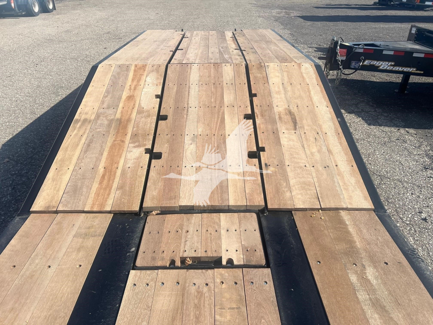 Lowboy trailer deck with wooden planks and metal reinforcement showing split plywood sections and central access hatch.