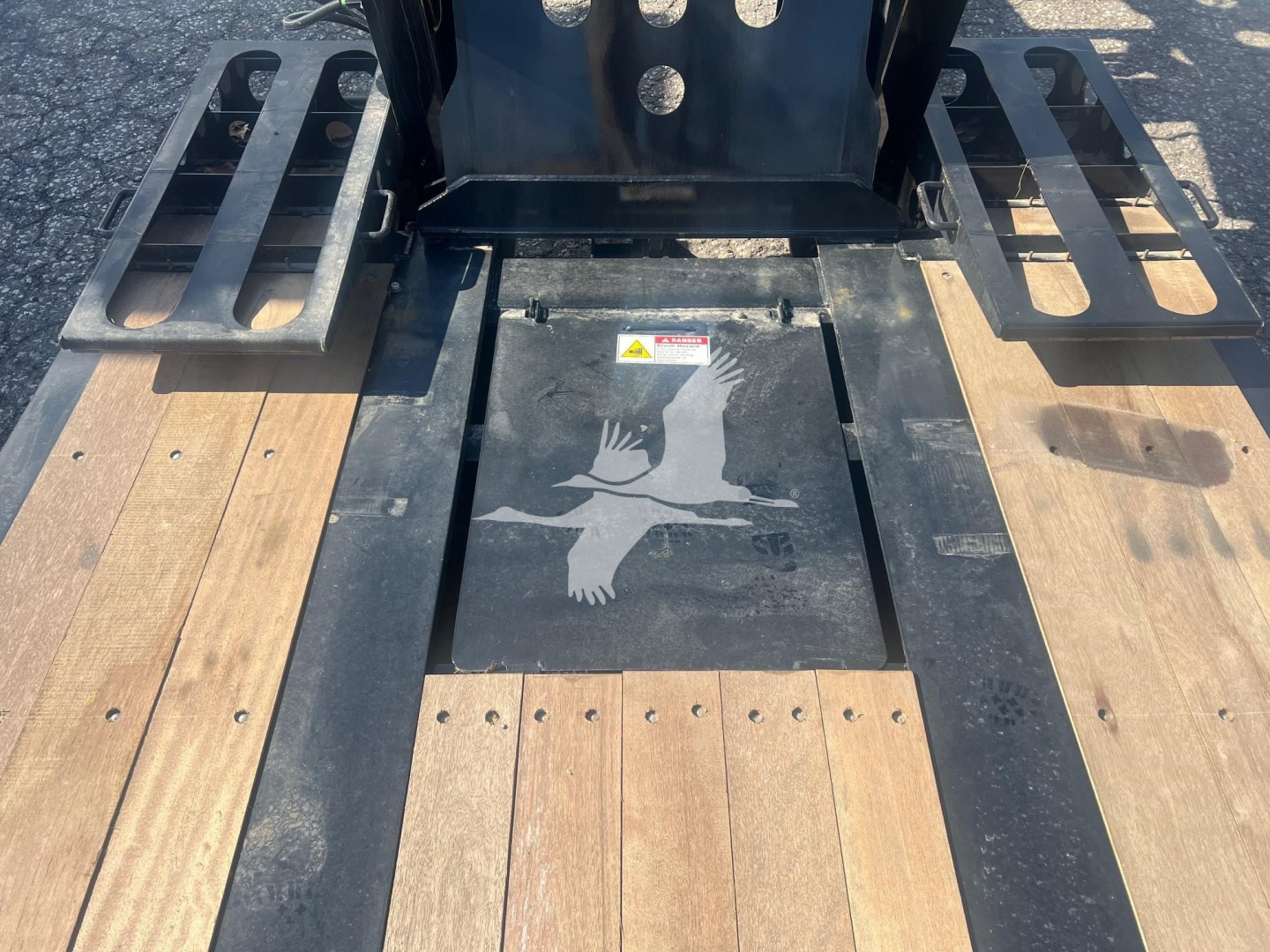 Fontaine paver Pro trailer deck with wood planks and metal ramp platforms; central access hatch with warning label and hand graphic.