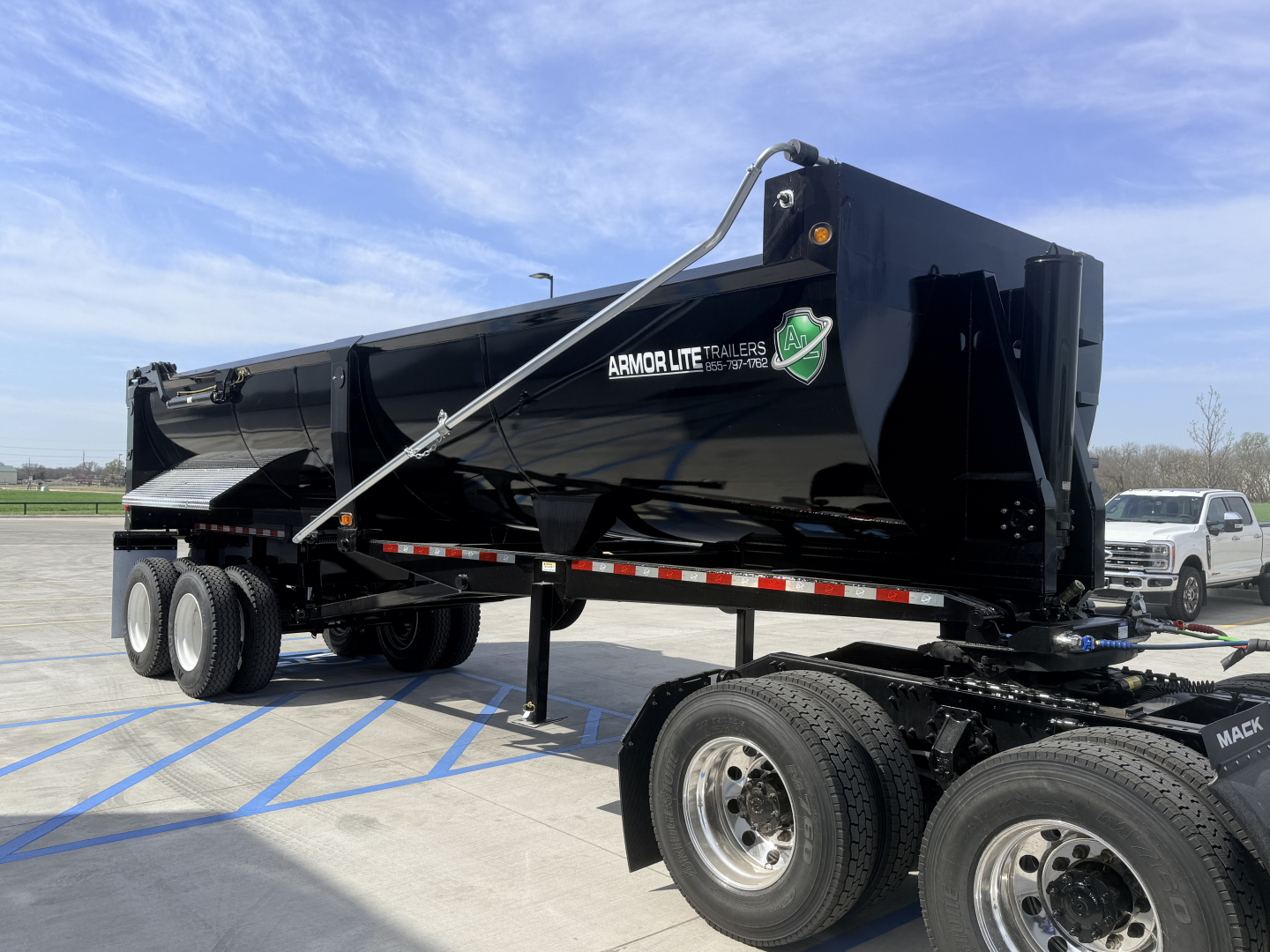 Armor Lite SHD 28/48 dump trailer in black with branding, single point hitch, dual rear axles, and front hitch stand visible.