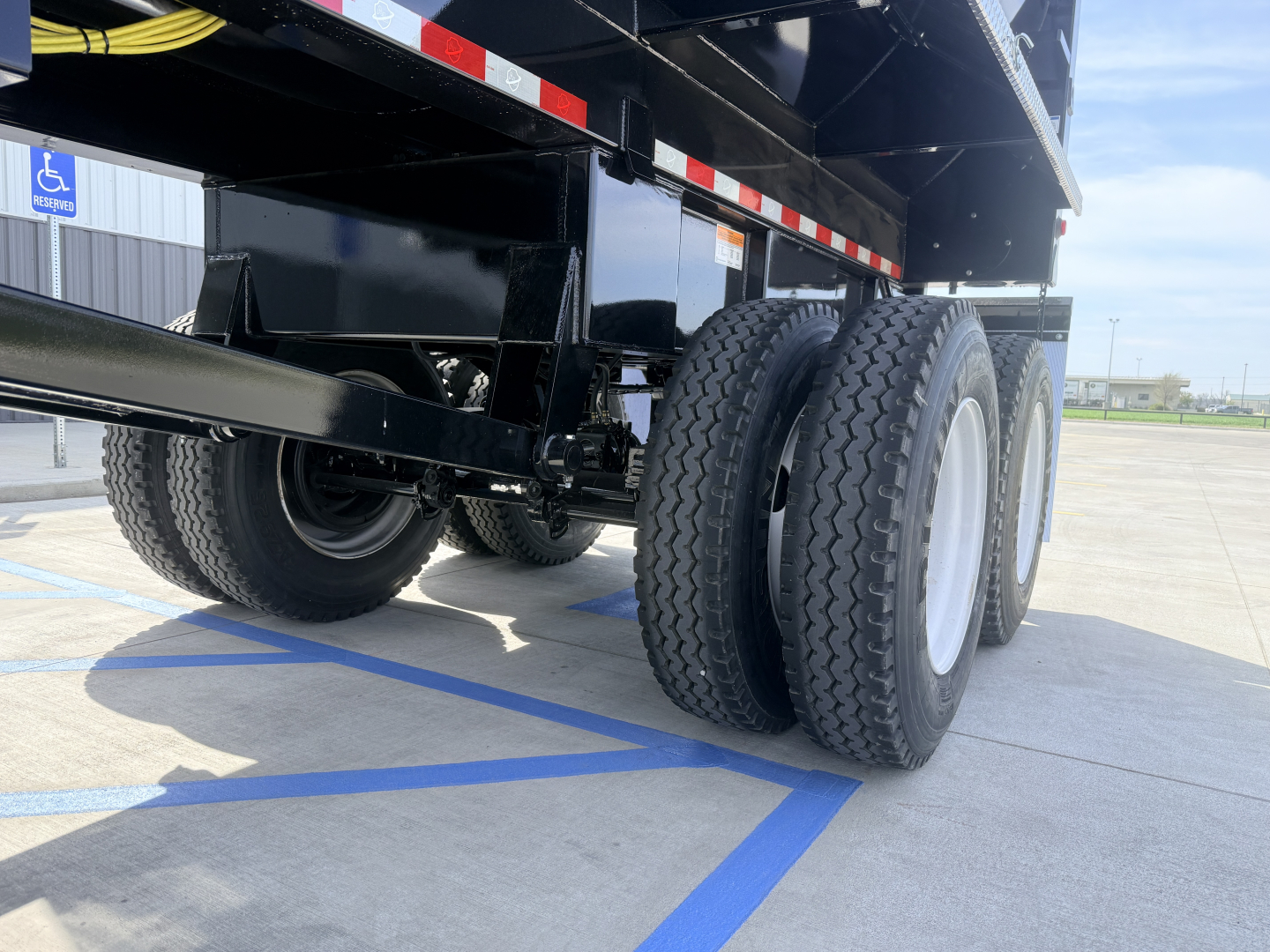 Dump trailer undercarriage showing dual rear tandem wheels and black steel frame with reflective tape.