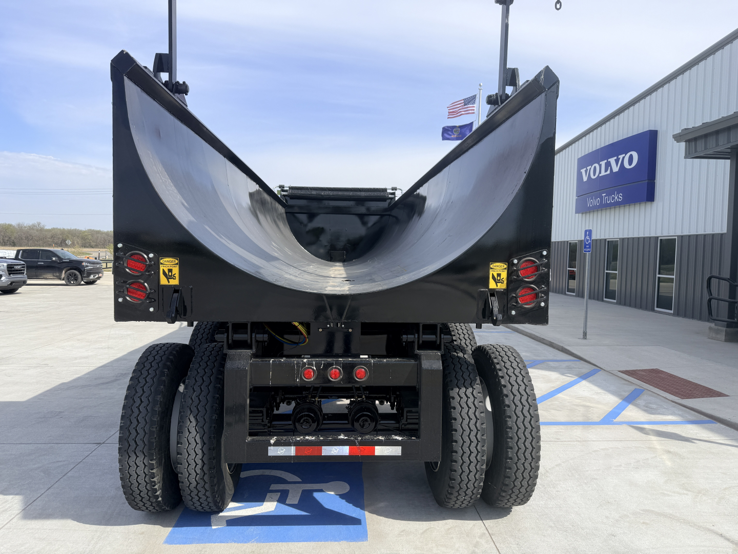 Dump trailer rear view with open tailgate, dual rear axles, taillights, and chassis components visible.