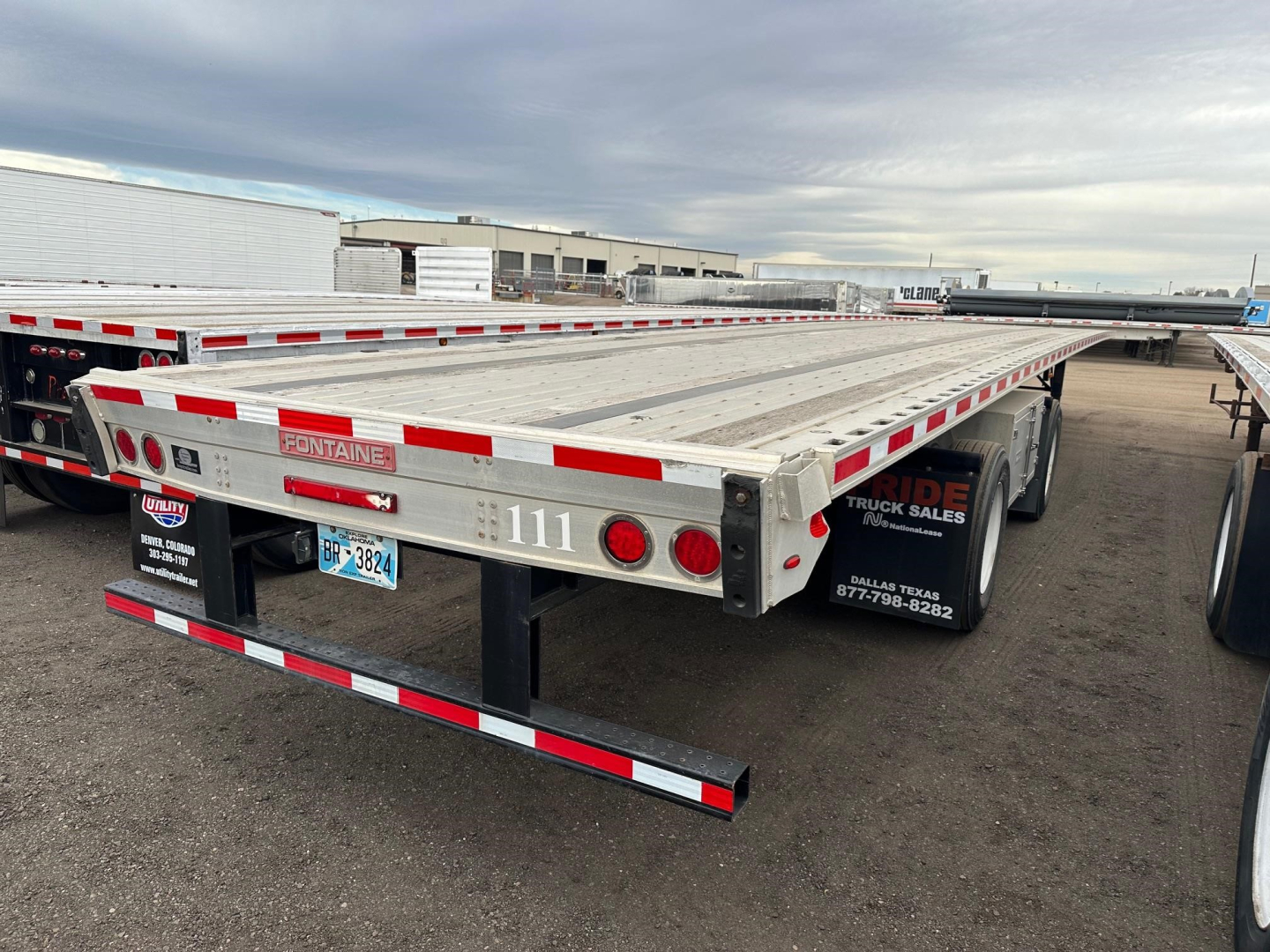 Flatbed trailer in a yard showing Fontaine branding, rear tail lights, bumper with white and red reflective tape, and stock number 111 on the side.