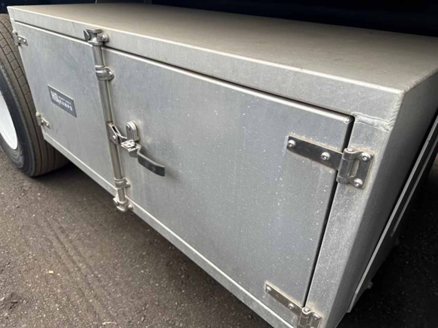 Flatbed trailer storage box mounted under Fontaine Infinity trailer showing steel toolbox with latch and hinges.