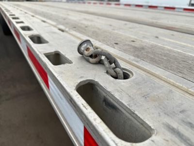 Flatbed trailer deck with chained drop hook anchor and sloted tie-down holes.