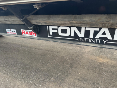Trailer side with Fontaine Infinity branding showing 'Fontaine Infinity' decal and a fuel/rash sticker; low-angle view of step and frame.