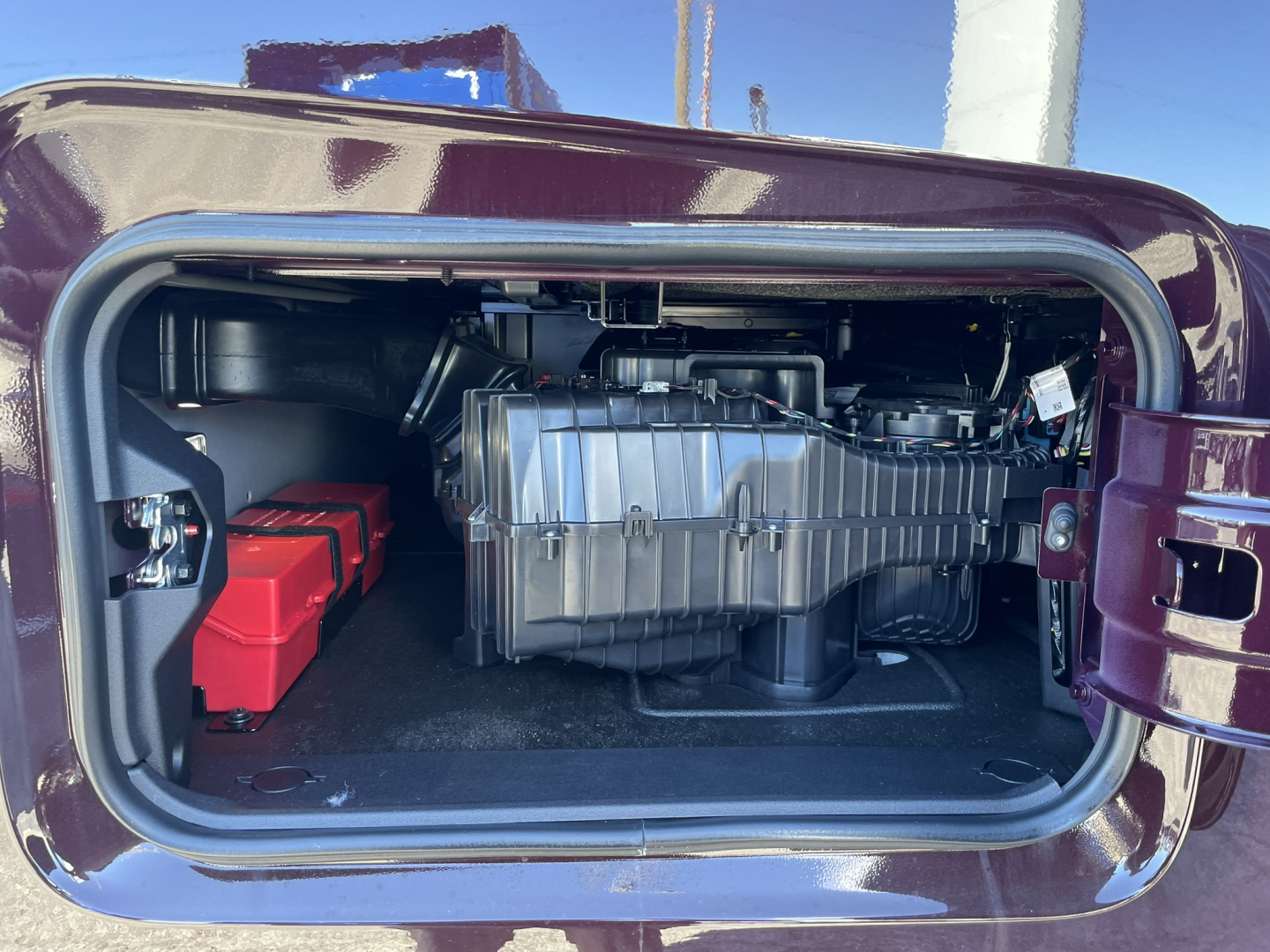 Truck engine bay showing large silver turbo housing and red battery in storage area inside a recessed compartment.
