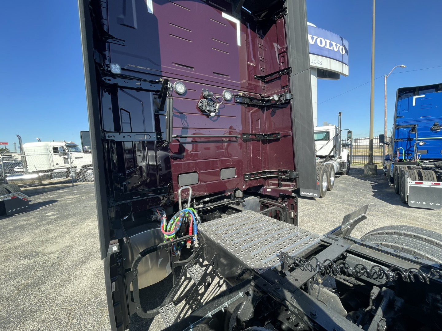 Volvo VNL64T860 truck rear cab area showing electrical harnesses and platform, maroon paint, exterior chrome steps, and chassis in a dealership lot.