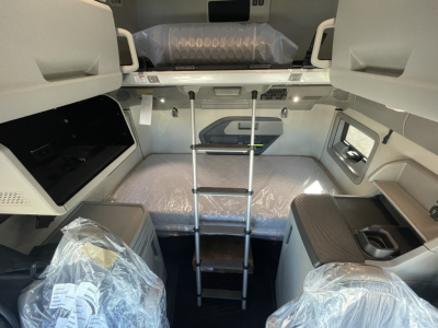 Volvo VNL64T860 cab interior showing bunk bed with ladder, overhead storage, and windowed side wall. Plastic-wrapped seating and components visible.