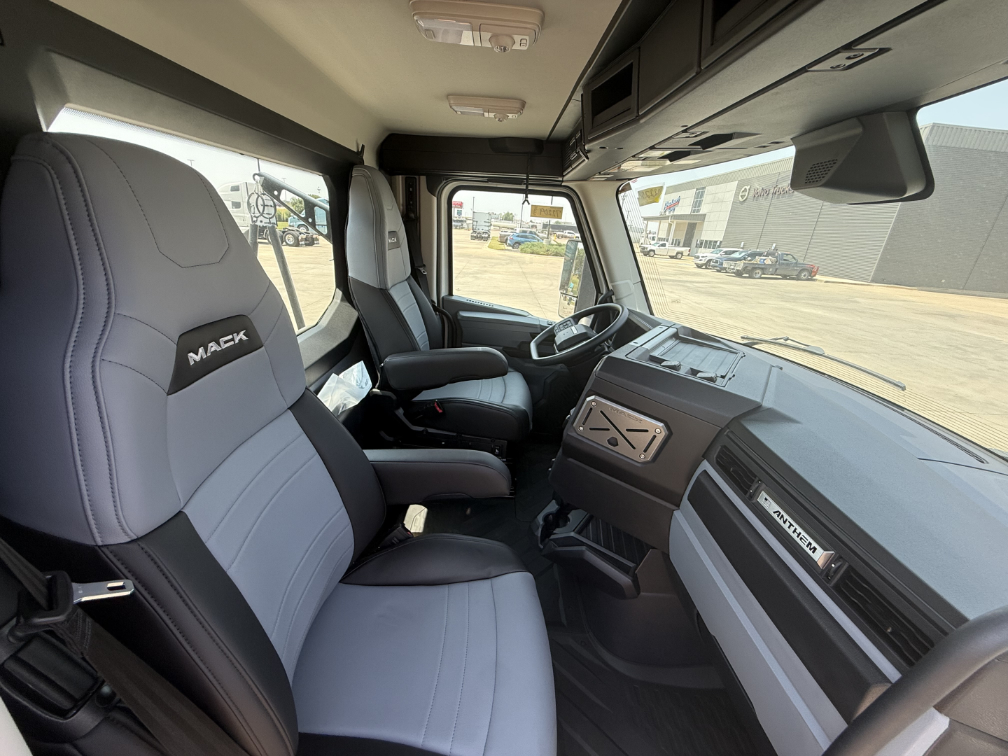 Interior of 2027 Mack AN64T cab showing driver and passenger seats with Mack branding, dashboard, steering wheel, and overhead storage.