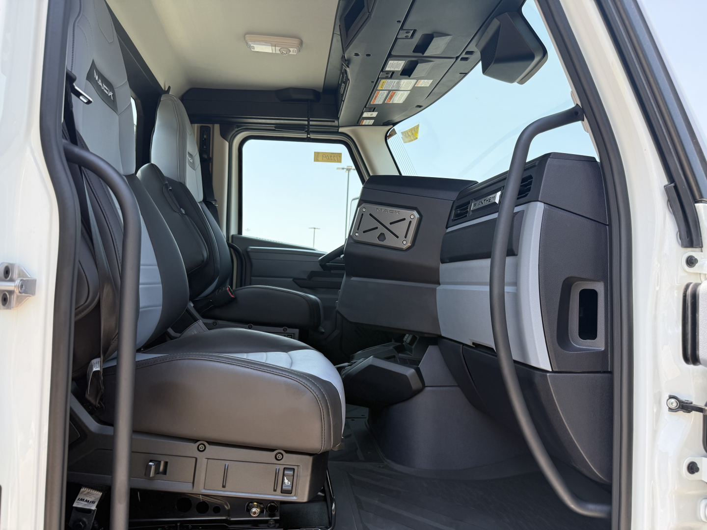 Interior view of a new 2027 Mack AN64T daycab truck cab, showing the driver seat, passenger seat, dashboard, steering column, and center console.