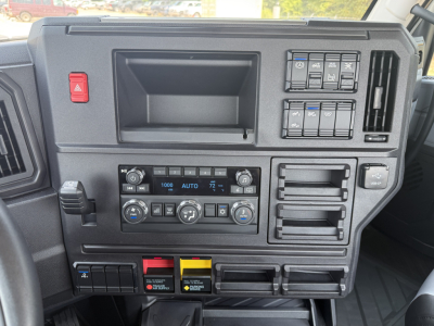 Dashboard of a 2027 Mack AN64T showing center climate controls, multiple switches, and storage pockets.