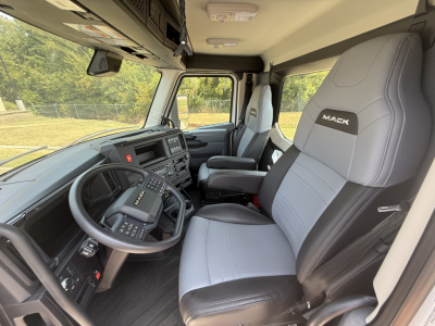 Interior of a new Mack AN64T daycab showing steering wheel, driver seat with Mack logo, large dashboard, and front passenger seat in a right-hand drive? Capacities not visible. 