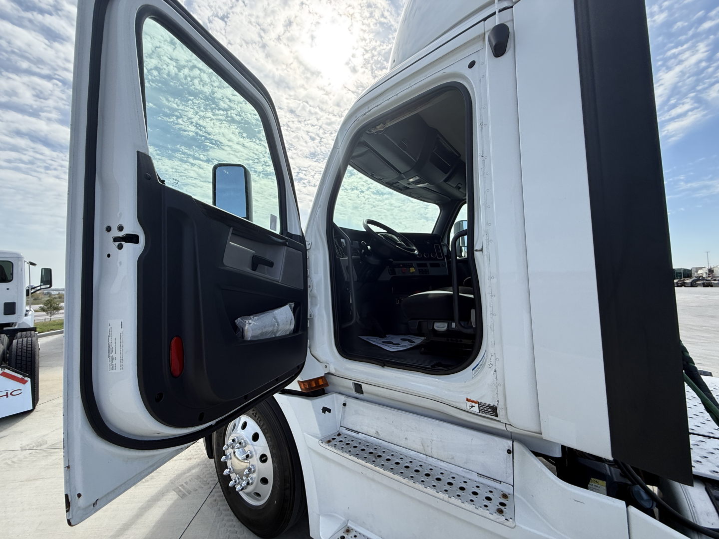 Truck cab doorway with open door, interior visible, step with metal tread, underside of cab, side mirror, and part of the steering wheel visible.
