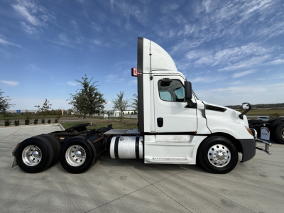 White Freightliner PT126064S daycab tractor side view showing fuel tanks and dual rear axles.