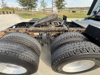 Front view of Freightliner cabless tractor chassis showing dual rear axles and mud/dirt on tires, exposed fifth wheel area and drive line components.