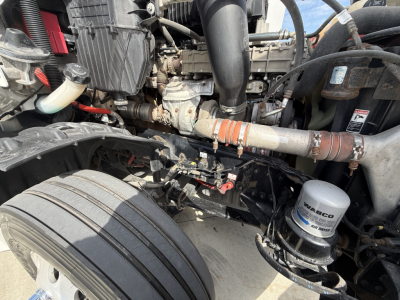 Truck engine bay showing air filter, hoses, exhaust pipe, coolant reservoir, and starter motor; visible components include belts, wiring, and a Warco fuel/air filter canister.